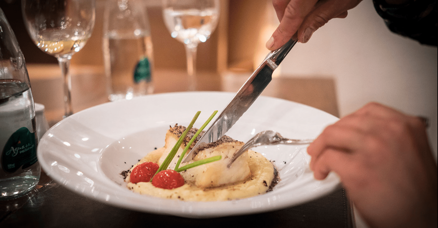 A person cuts a piece of fish on a plate.