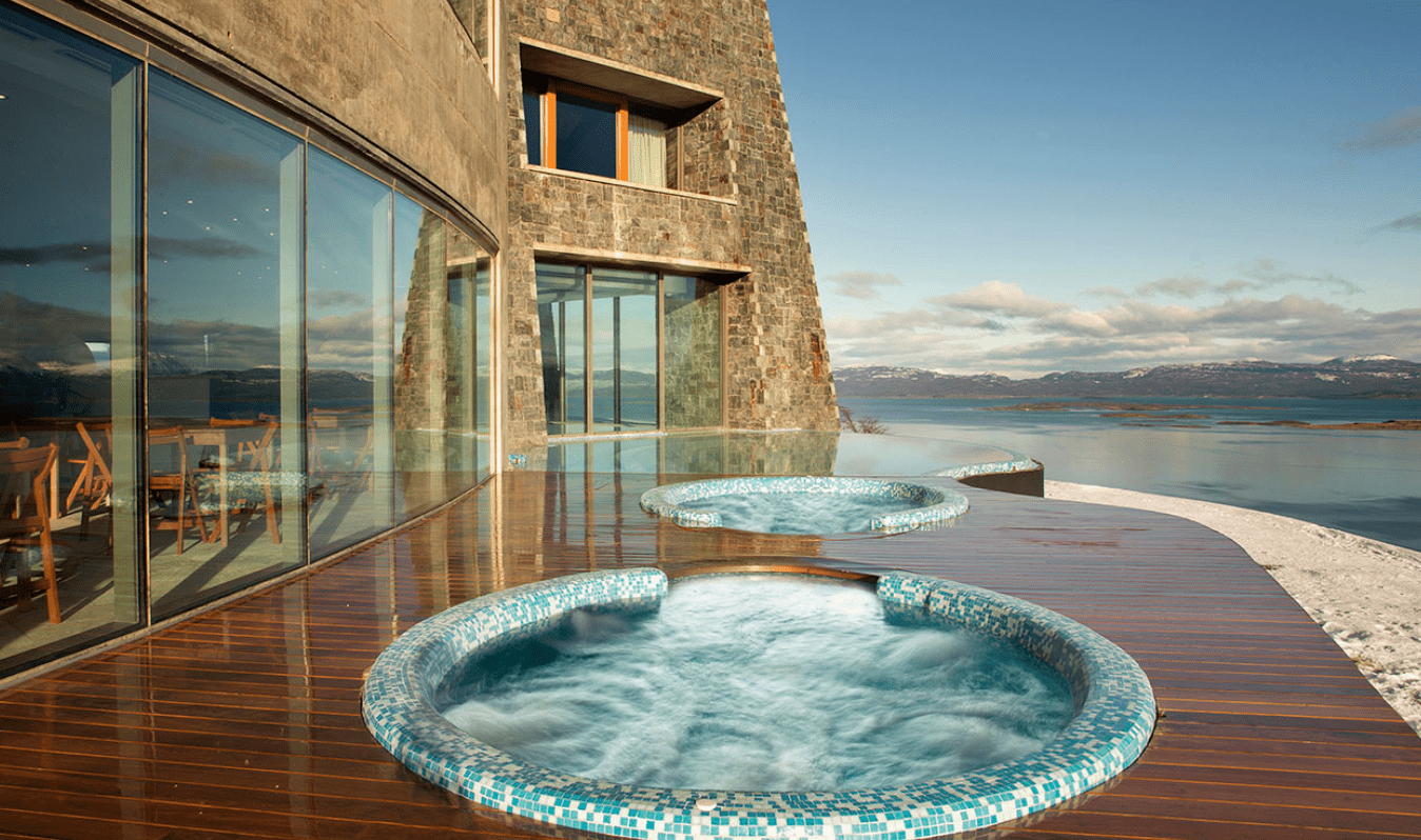 Two hot tubs on a wooden deck overlooking water.