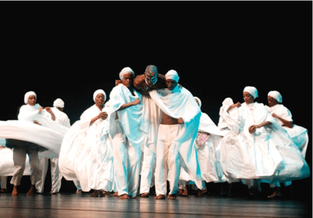 Group of dancers in white costumes on stage.