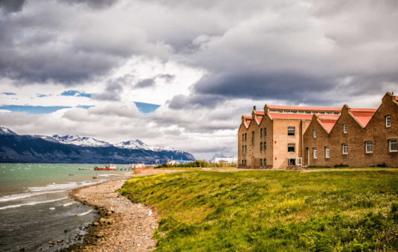 Brick building by a lake and mountains.