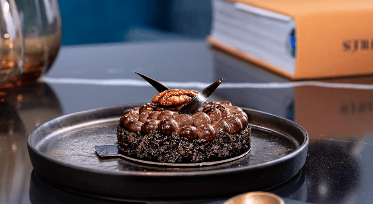 Chocolate pecan tart on black plate.