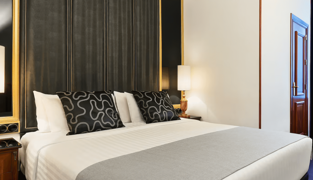 White bed with patterned pillows in hotel room.