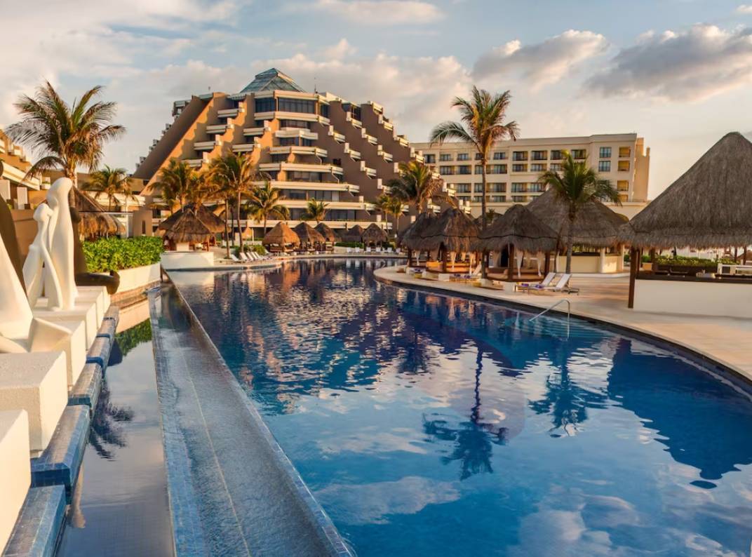 Resort pool with palm trees and buildings.