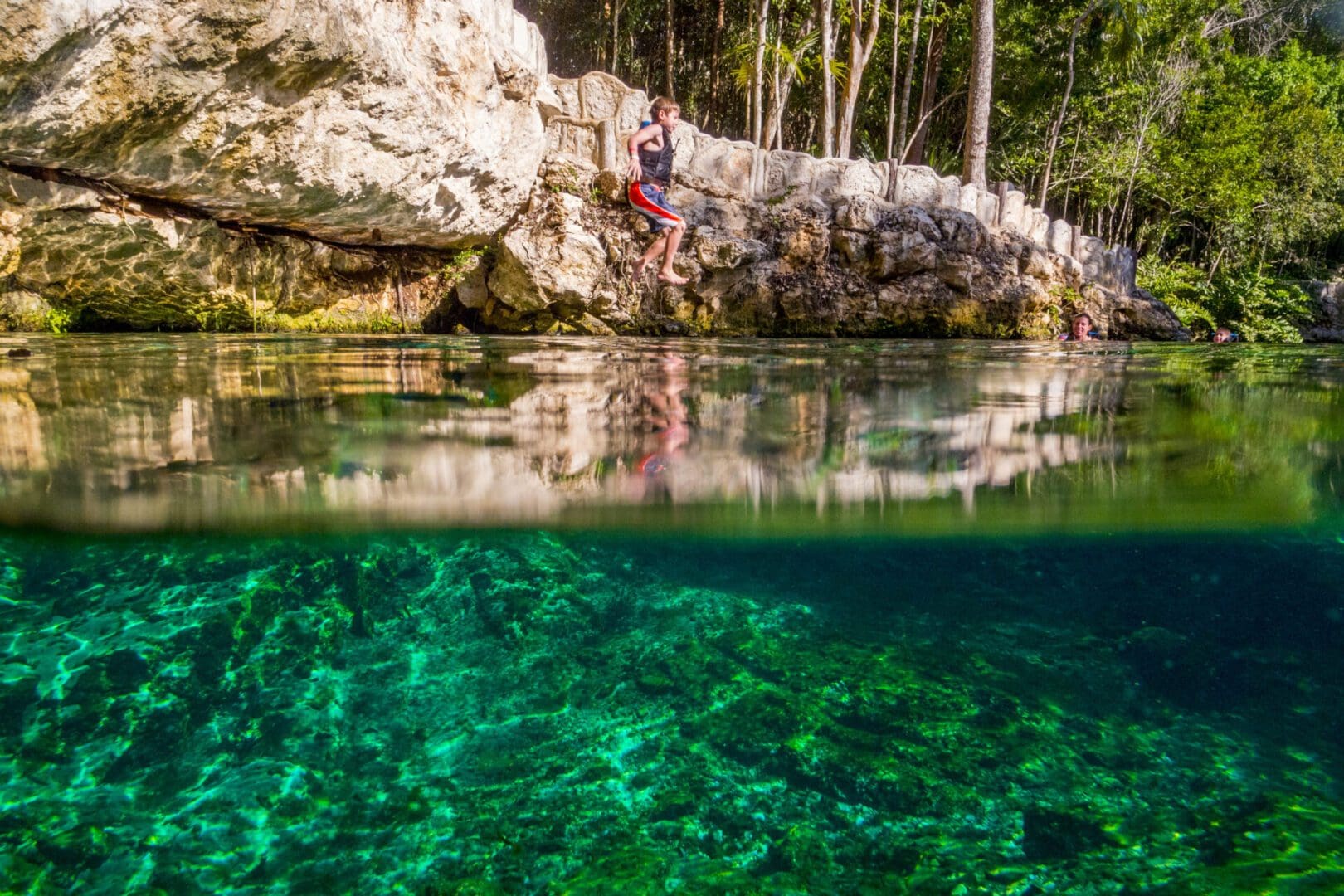 Boy jumping into clear cenote water.