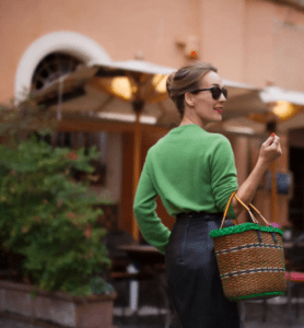 A woman wearing a green sweater and black skirt holding a wicker basket.