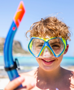 A young boy wearing a snorkel and goggles on the beach.