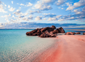 A beach with pink sand and rocks in the background.