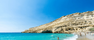 A beach with cliffs and people swimming in the water.