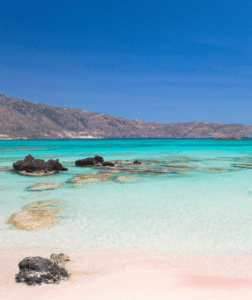 A beach with turquoise water and rocks in the background.