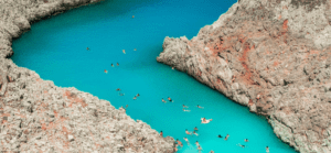 People are swimming in the blue water of a cliff.