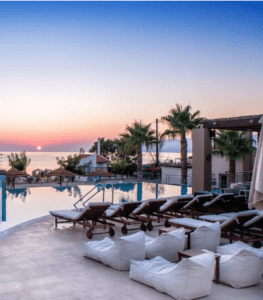 A pool with lounge chairs and a beach in the background.