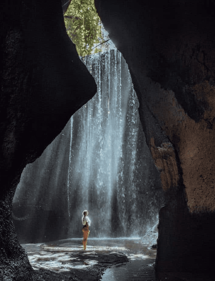 Woman standing by waterfall in cave.