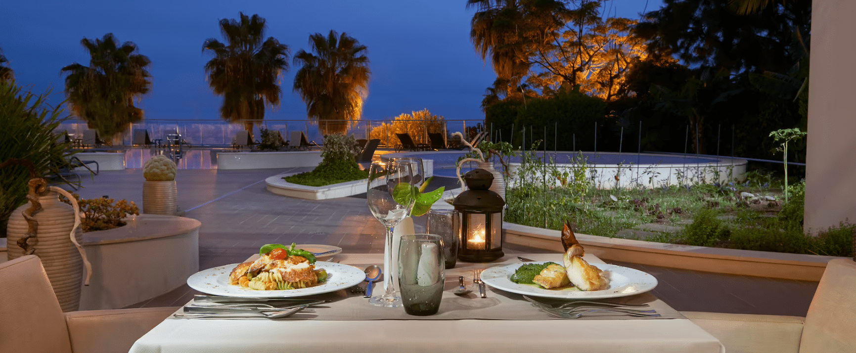 Two plates of food are set on a table in front of a pool.