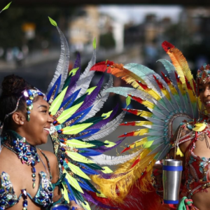 Two women dressed in colorful feathers are walking down the street.