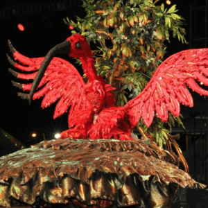 A red flamingo is sitting on top of a tree.