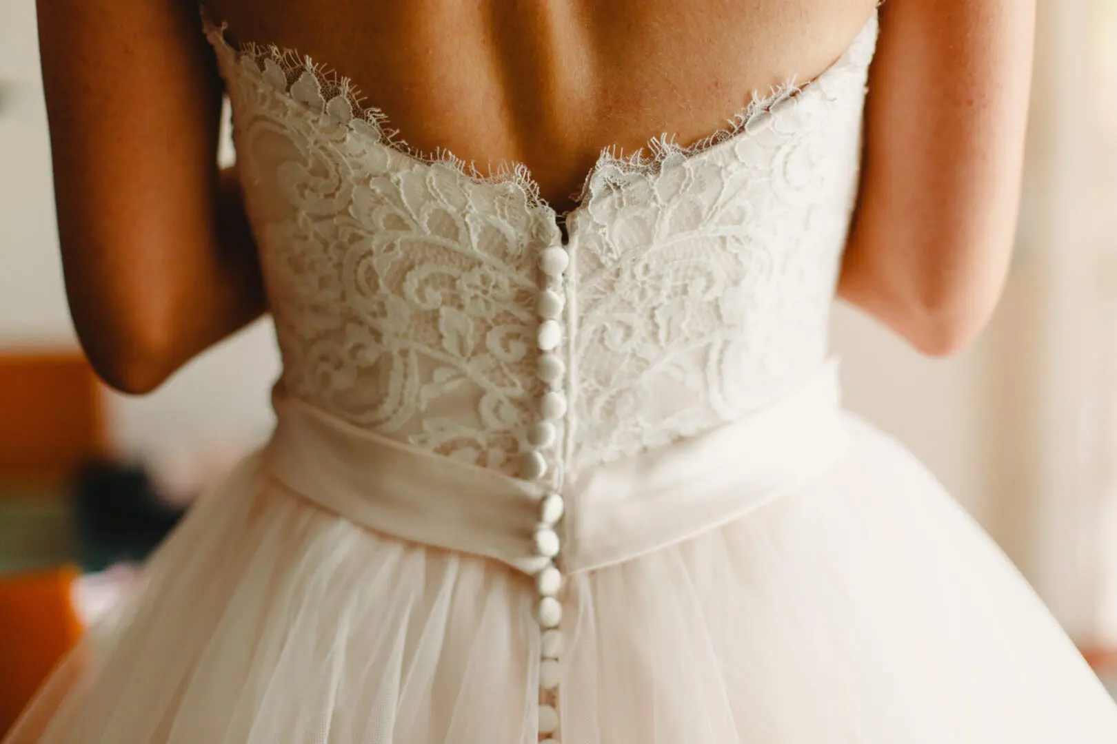 Bride getting ready, they help her by buttoning the buttons on the back of her dress.