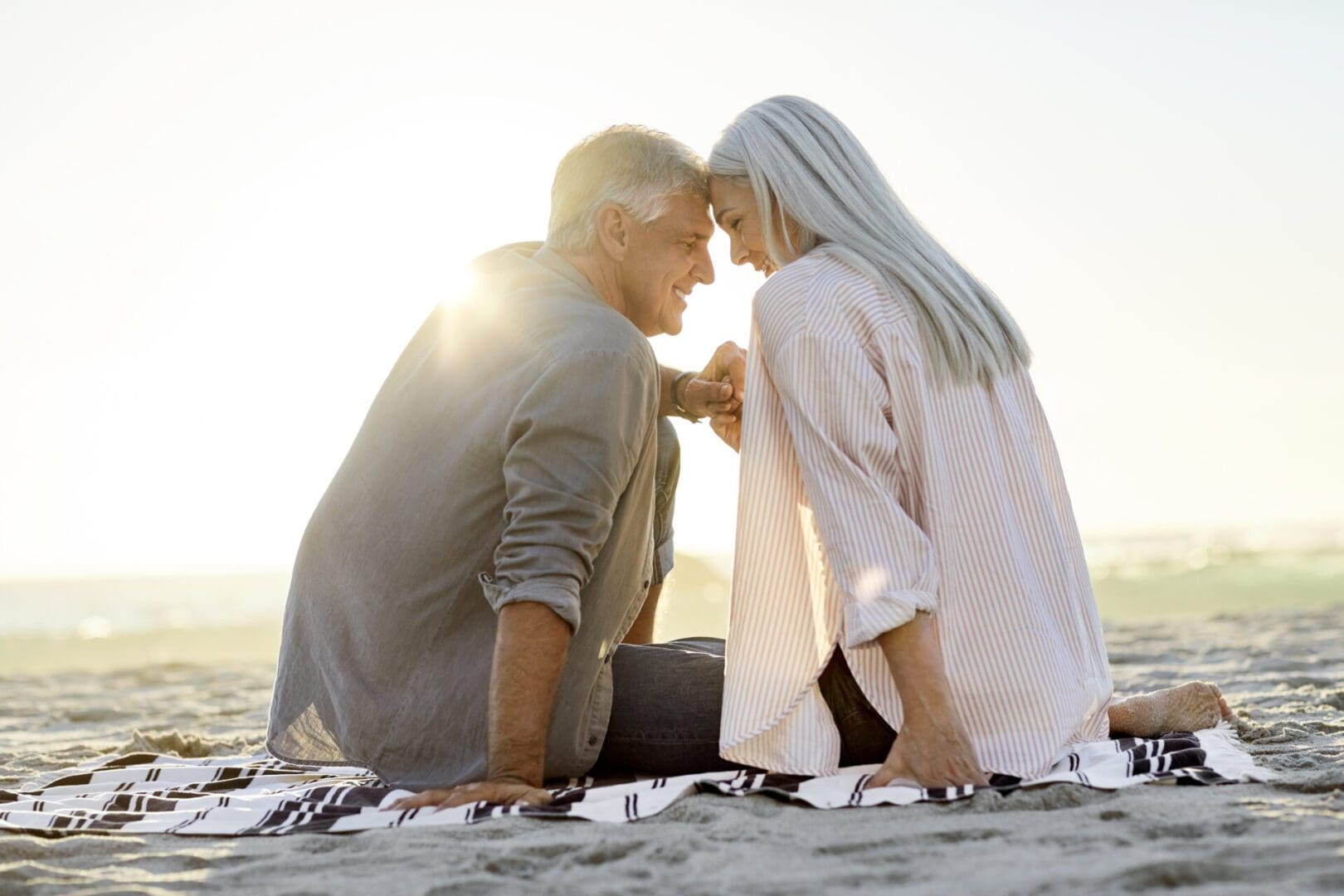 Senior couple cuddling on beach blanket.