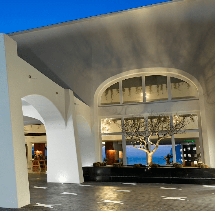 Modern hotel lobby with arched windows and a tree.