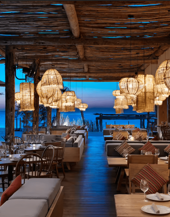 Beachfront restaurant with woven lights and wooden tables.