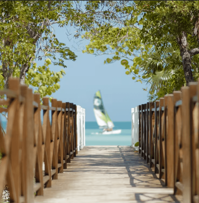 Wooden walkway to a beach with a sailboat.