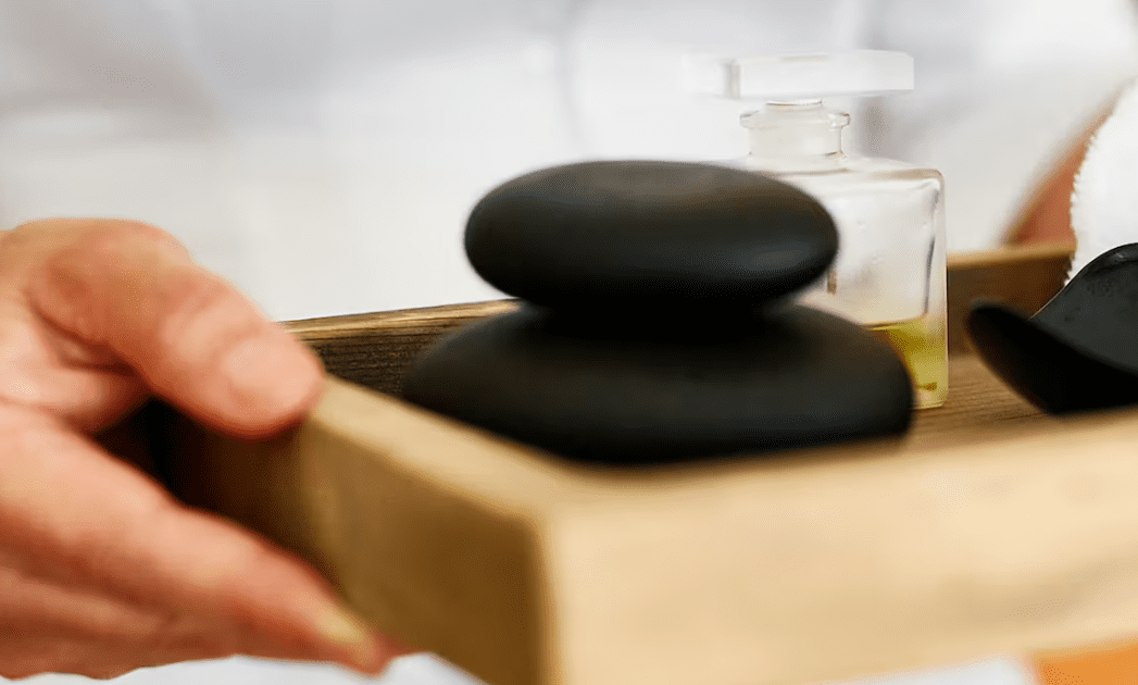 Hand holding tray with hot stones and oil.