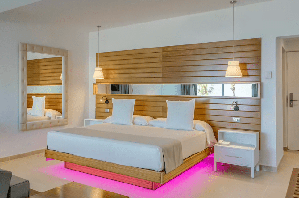 White bed with pink light in hotel room.