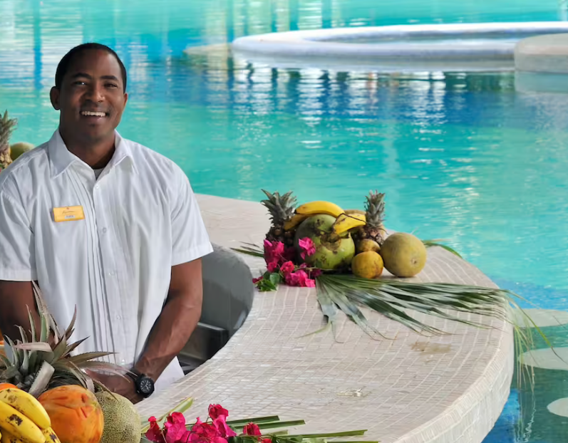 Smiling man by pool with fruit platter.