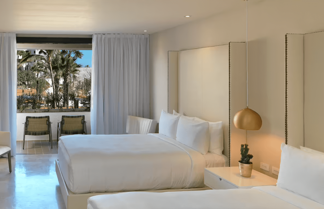 White hotel room with two beds and patio view.