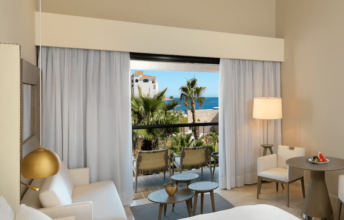 Ocean view room with white couch and chairs.