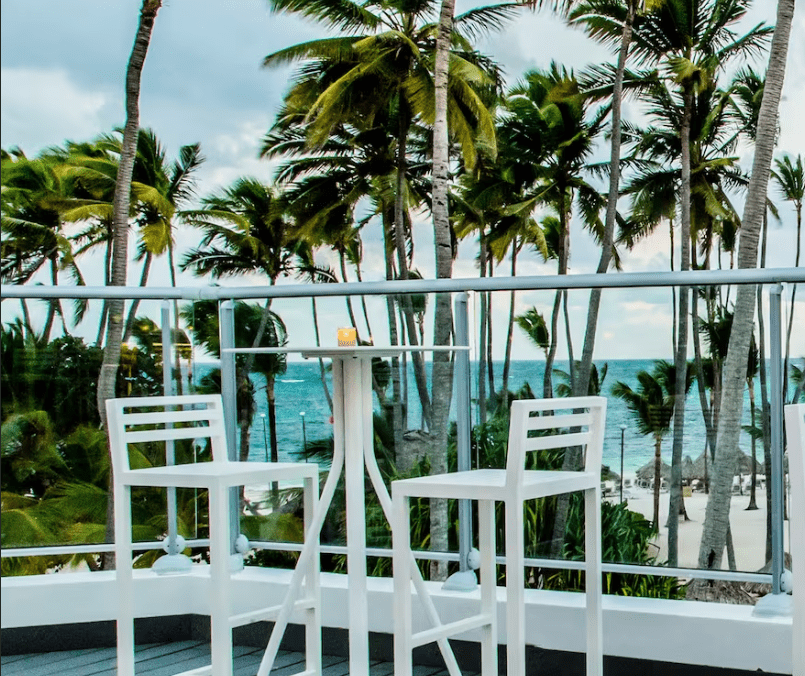 White chairs and table on balcony overlooking beach.