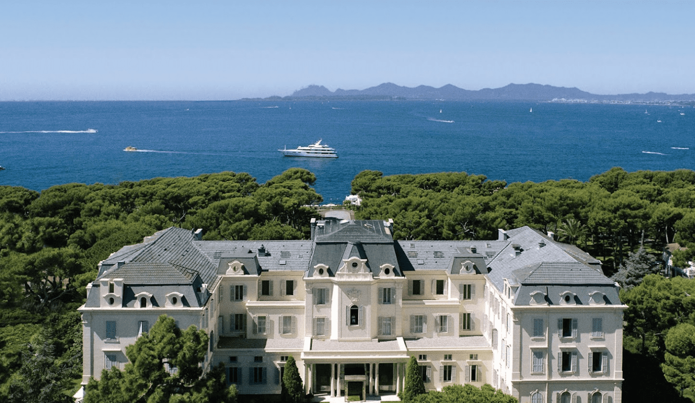 An aerial view of a white mansion near the ocean.