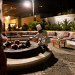 Man in white prepares food outdoors.