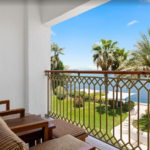 Balcony with chairs overlooking water and palms.