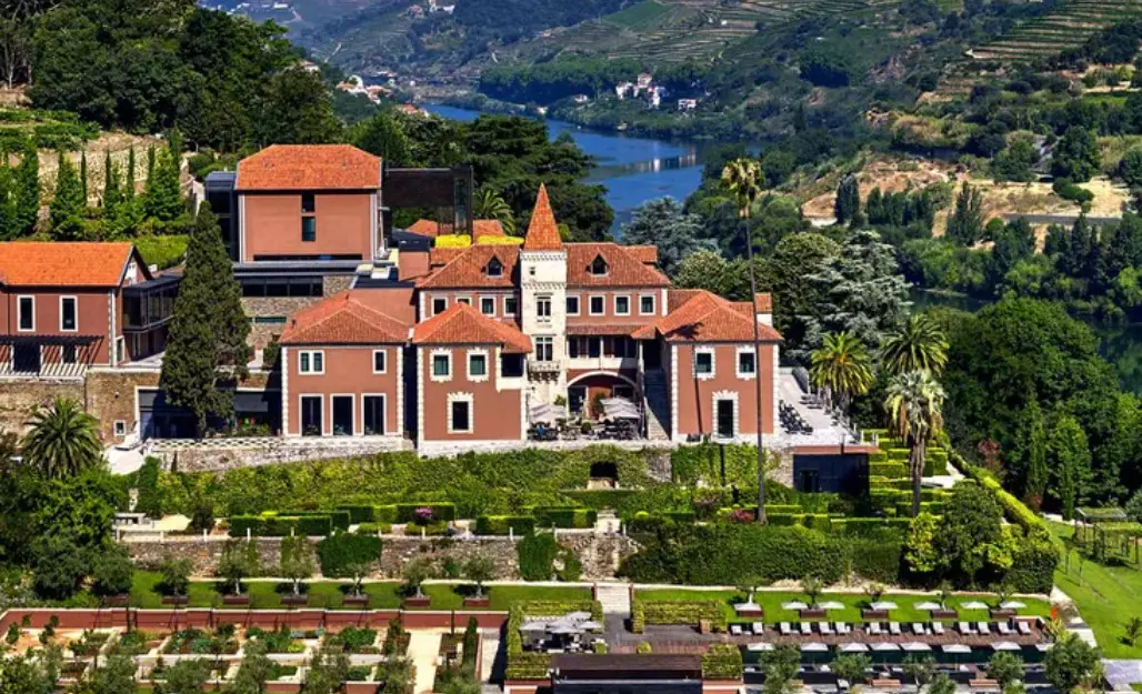 Red-roofed hotel with river view and gardens.