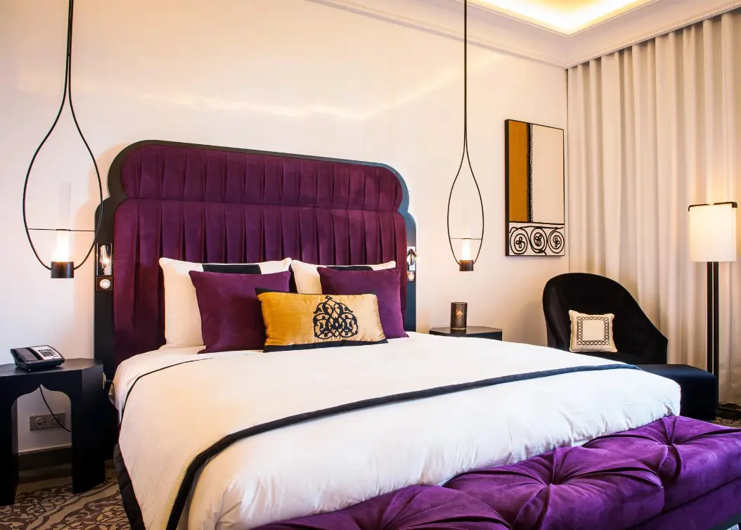 A purple and white hotel bed with a lamp.