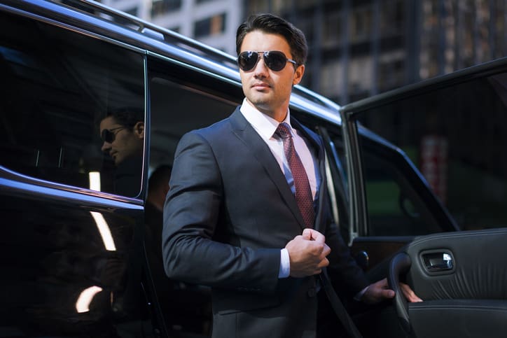 Handsome young businessman arriving in executive car wearing a suit and sunglasses in a city