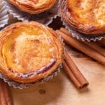 Pastel de nata tarts and cinnamon sticks on wooden tray. Top view.