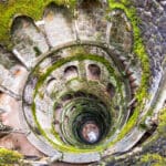 Moss-covered stone spiral staircase in ruins.