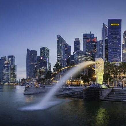 "Singapore, Singapore - 14th February 2012: The crowded cityscape of Central Business District skyscrapers overlooking the Merlion fountain on the Marina Bay waterfront at dusk as tourists and locals enjoy the warm evening promenade, Singapore. Composite panoramic image created from six contemporaneous sequential photographs."